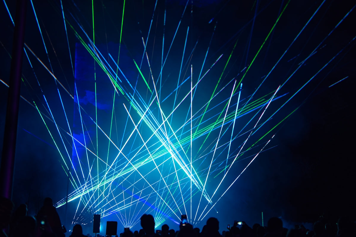 Blue and green lasers illuminate a dark concert venue.